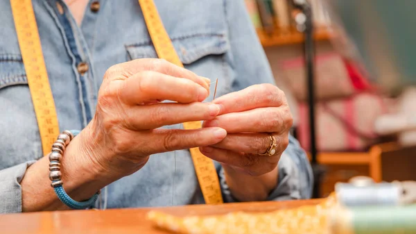 hands of an old woman threading a sewing needle. horizontal