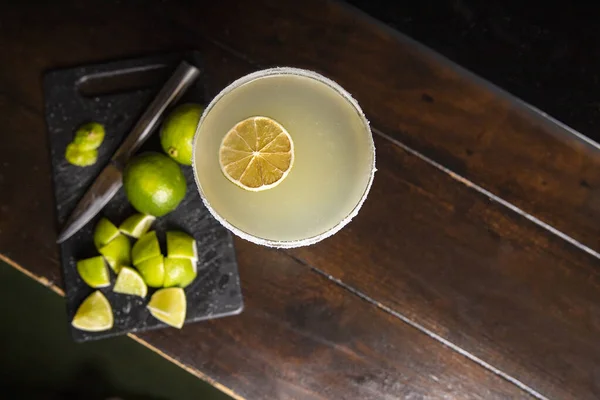 Still life with zenith plane of a margarita cocktail surrounded by pieces of lime on a wooden surface. horizontal