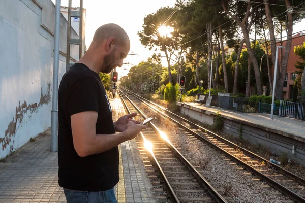 profile man standing at a train station looks at his mobile phone. horizontal