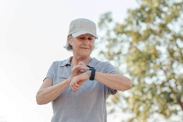 seventy-year-old woman looks at her outdoor sports watch. horizontal