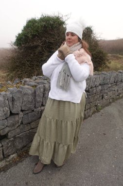 Kış boyu etek giyen, beyaz kazaklı ve beyaz şapkalı atkı takan bir kadın kendini sıcak tutmak ve doğada dinlenerek zaman geçirmek için... 