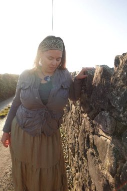 Kırsaldaki taş duvarın yanında duran kadın hayatı düşünüyor.