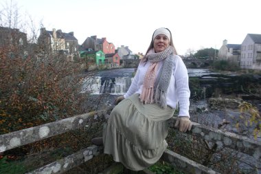 Ennistymon Şelalesi 'nde, ahşap korkuluklarda oturan bir model kışın manzaraya hayran kalır.