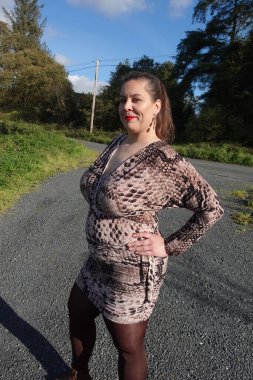 Kadın yılan desenli bir elbise giyiyor ve güneşten hoşlanıyor. 