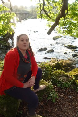 Güneşli bir günde nehir kıyısında oturan bir kadın.