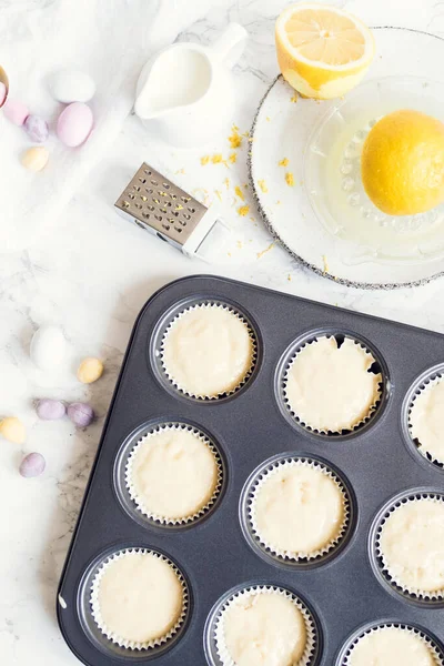 Hazırlık süreci, beyaz mermer arka planda mini çikolatalı yumurtalarla süslenmiş Paskalya kekleri. Mutlu Paskalyalar. Üst görünüm.