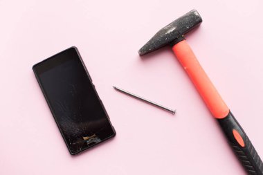 Çekiç, çivi ve cep telefonu pembe arka planda kırılmış. Düşmüş akıllı telefon konsepti. Üst görünüm.