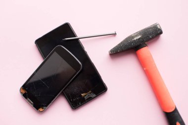 Çekiç, çivi ve cep telefonu pembe arka planda kırılmış. Düşmüş akıllı telefon konsepti. Üst görünüm.