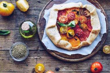 Taze domatesli ve ahşap masadaki fesleğenli tuzlu galette. Vejetaryen sağlıklı gıda konsepti. Üst görünüm.
