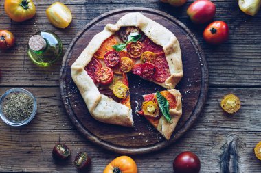Taze domatesli ve ahşap masadaki fesleğenli tuzlu galette. Vejetaryen sağlıklı gıda konsepti. Üst görünüm.