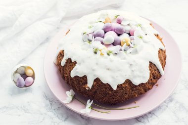 Çiçeklerle süslenmiş paskalya pastası ve beyaz mermer arka planda mini çikolata yumurtaları. Mutlu Paskalyalar..