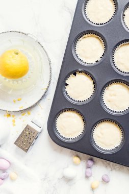 Hazırlık süreci, beyaz mermer arka planda mini çikolatalı yumurtalarla süslenmiş Paskalya kekleri. Mutlu Paskalyalar. Üst görünüm.