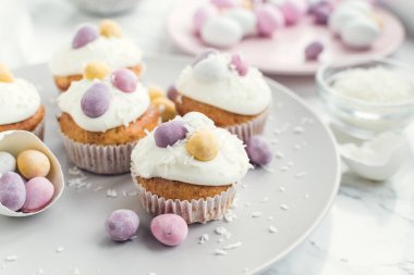 Beyaz mermer arka planda mini çikolatalı yumurtalarla süslenmiş Paskalya kekleri. Mutlu Paskalyalar..