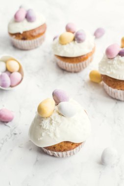 Beyaz mermer arka planda mini çikolatalı yumurtalarla süslenmiş Paskalya kekleri. Mutlu Paskalyalar..