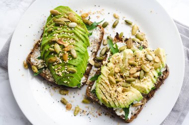 Kahvaltı veya çavdar ekmeği, avokado, roka, kabak ve susam, tuz ve biber dilimlenmiş ile öğle yemeği için sağlıklı avokado kızartır. Vejetaryen sandviç. Bitki temelli diyet. Temiz yemek. Üstten görünüm.