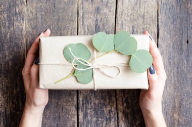 Okaliptüs dalı ile süslenmiş kahverengi kağıda sarılmış hediye kutusu, doğal çevre dostu sıfır atık paketleme fikri. Üst görünüm.
