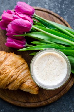 Bir fincan kahve, pembe laleler ve siyah arka planda kruvasan. Sevgililer Günü, Anneler, Kadınlar Günü sabahı konsepti. Sevgililer Günü kahvaltısı. Üst görünüm.