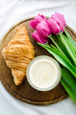Bir fincan köpüklü kahve ve beyaz yatak balayında pembe laleler. Anneler Günü 'nde, Sevgililer Günü' nde ya da Kadınlar Günü 'nde kahvaltı. Yatakta romantik sabah konsepti sürprizi. Üst Manzara. Boşluğu kopyala.