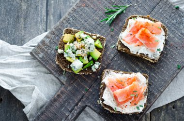 Sağlıklı kahvaltı. Tahtada çavdar ekmeği, avokado, somon ve krem peynirli tost. Sağlıklı atıştırmalık konsepti. Üst görünüm.