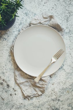 Boş beyaz tabak, çatal ve gri keten peçete beton arka planda metin için yer var. Yemek arkaplanı. Güzel anlaşma. Menü modeli. Düz yatıyordu. Üst Manzara. Boşluğu kopyala.