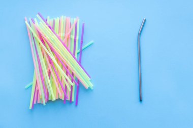 Birçok plastik pipet, yeniden kullanılabilir bir metale karşı mavi arka planda pipet içiyor. Sıfır sürdürülebilir yaşam, plastiksiz konsept. Eko dostu plastik eşyalar. Üst görünüm.