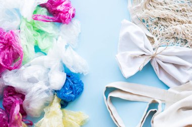 Birçok tek kullanımlık plastik torba mavi arka planda tekrar kullanılabilir pamuk torbalara karşı. Sıfır atık. Sürdürülebilir yaşam, plastiksiz konsept. Eko dostu plastik eşyalar. Üst görünüm.