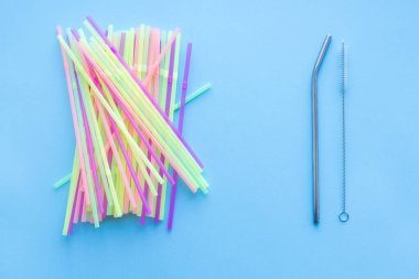 Birçok plastik pipet tekrar kullanılabilir bir metale karşı pipet içer ve mavi arka planda saman içer ve temizlik fırçası temizler. Sıfır sürdürülebilir yaşam, plastiksiz konsept. Eko dostu plastik eşyalar. Üst görünüm