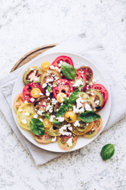 Feta peyniri, fesleğen ve zeytinyağlı renkli domateslerden taze domates salatası. Vejetaryen ve vejetaryen yemekleri. Lezzetli ve sağlıklı bir yemek konsepti. Üst Manzara. Boşluğu kopyala.