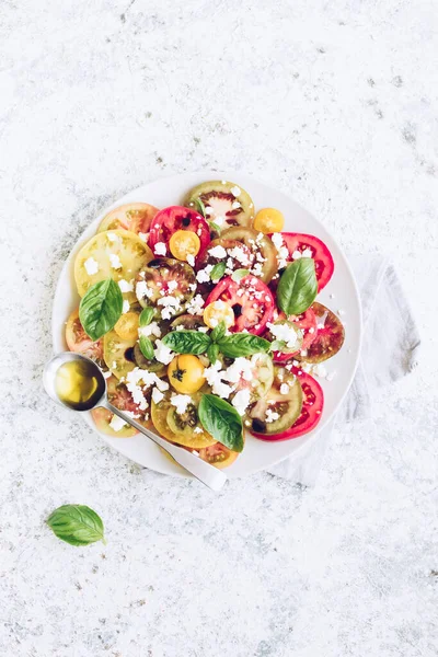 Feta peyniri, fesleğen ve zeytinyağlı renkli domateslerden taze domates salatası. Vejetaryen ve vejetaryen yemekleri. Lezzetli ve sağlıklı bir yemek konsepti. Üst Manzara. Boşluğu kopyala.