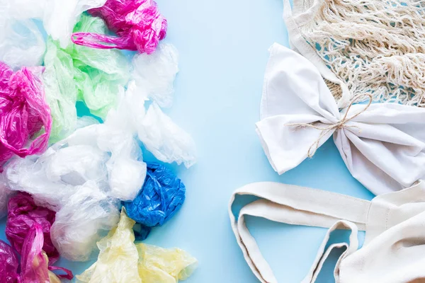 Birçok tek kullanımlık plastik torba mavi arka planda tekrar kullanılabilir pamuk torbalara karşı. Sıfır atık. Sürdürülebilir yaşam, plastiksiz konsept. Eko dostu plastik eşyalar. Üst görünüm.