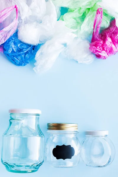 Birçok tek kullanımlık plastik torba mavi arka planda yeniden kullanılabilir cam kavanozlara karşı. Sıfır atık. Sürdürülebilir yaşam, plastiksiz konsept. Eko dostu plastik eşyalar. Üst görünüm.