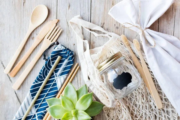 Sıfır atık. Pamuk torbaları, cam kavanoz, bambu çatal bıçak takımı ve tahta arka planda diş fırçası. Sürdürülebilir yaşam. Eko dostu plastik eşyalar. Üst görünüm.