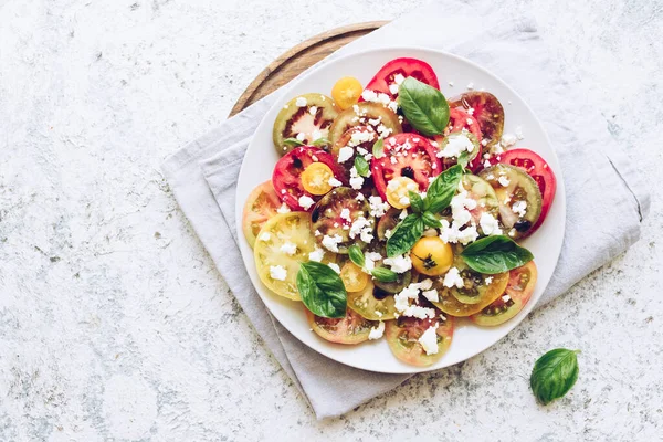Feta peyniri, fesleğen ve zeytinyağlı renkli domateslerden taze domates salatası. Vejetaryen ve vejetaryen yemekleri. Lezzetli ve sağlıklı bir yemek konsepti. Üst Manzara. Boşluğu kopyala.