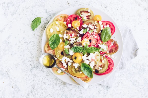 Feta peyniri, fesleğen ve zeytinyağlı renkli domateslerden taze domates salatası. Vejetaryen ve vejetaryen yemekleri. Lezzetli ve sağlıklı bir yemek konsepti. Üst Manzara. Boşluğu kopyala.