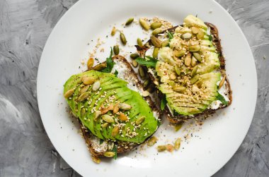 Kahvaltı veya çavdar ekmeği, avokado, roka, kabak ve susam, tuz ve biber dilimlenmiş ile öğle yemeği için sağlıklı avokado kızartır. Vejetaryen sandviç. Bitki temelli diyet. Temiz yemek. Üstten görünüm.