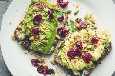 Kahvaltıda sağlıklı avokado tostları ya da öğle yemeğinde çavdar ekmeği, krem peynir, roka, dilimlenmiş avokado, kızılcık, balkabağı, kenevir ve susam tohumu. Vejetaryen sandviçler. Temiz yemek. Üst görünüm.