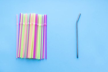 Birçok plastik pipet, yeniden kullanılabilir bir metale karşı mavi arka planda pipet içiyor. Sıfır sürdürülebilir yaşam, plastiksiz konsept. Eko dostu plastik eşyalar. Üst görünüm.