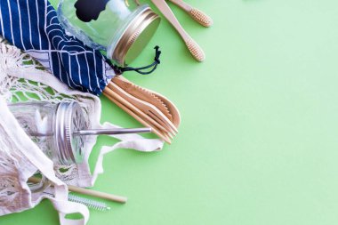 Sıfır atık. Pamuk torbası, bambu çatal bıçak takımı ve diş fırçası, cam kavanozlar, yeşil arka planda metal ve bambu pipetler. Sürdürülebilir yaşam. Eko dostu plastik eşyalar. Üst Manzara. Boşluğu kopyala.