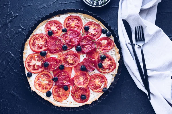 Vegetable tart with tomatoes, ricotta, black olives and thyme on black background. Vegetarian healthy food concept. Top view.