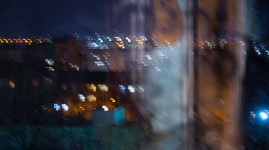 Gece mavisi şehir manzarası yansımalı bir pencereden geçiyor.