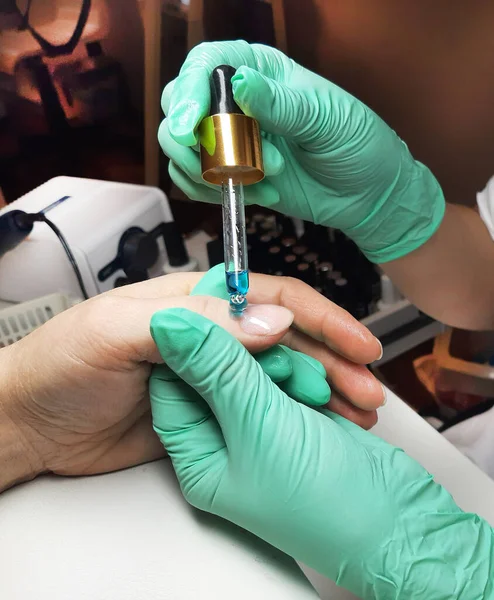 Yeşil lastik eldivenli bir ustanın kadın elleri derisinde pipet olan yağlar sürerler. Mükemmel bir manikür işlemi. Dosya manikürü konsepti. öğretim.