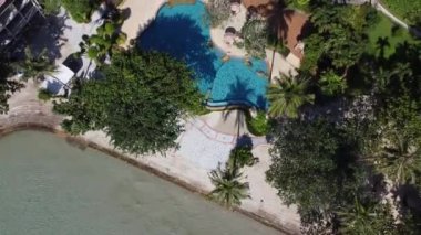 Bir dron, okyanus dalgalarına bakan parlak mavi bir yüzme havuzu üzerinde uçar..