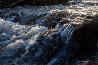 Su güneşte taştan akıntılar gibi akıyor..