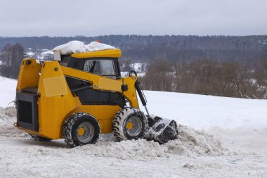Small orange forklift clearing snow from the street.