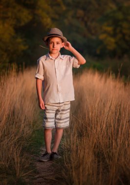 Şapkalı yakışıklı bir çocuk köy yolunda oturuyor, kitap okumak için.