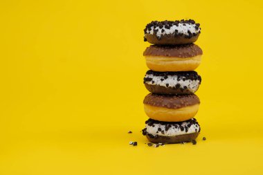 Sarı arka planda çikolatalı çörekler. Çörekler üst üste dizilmiş, kadınlar birbirlerinin üzerine çöreklerden kule tutuyorlar.