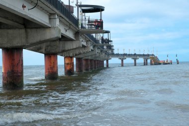 Denize kadar uzanan bir köprü. Deniz manzarası çok güzel. Baltık Denizi... arka plan beyaz bir kumsal ve denize uzanan ahşap bir köprü ve uzakta dağlar var. Gökyüzünde büyük bulutlar oluşuyor.