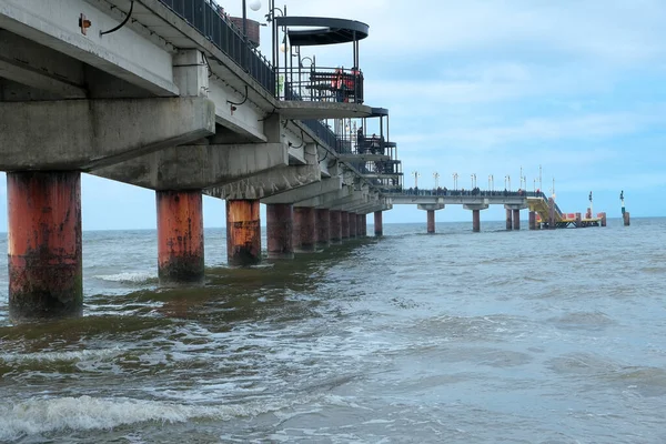 Denize kadar uzanan bir köprü. Deniz manzarası çok güzel. Baltık Denizi... arka plan beyaz bir kumsal ve denize uzanan ahşap bir köprü ve uzakta dağlar var. Gökyüzünde büyük bulutlar oluşuyor.