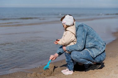 Mutlu baba ve onun sevimli küçük kızı tropikal plajda eğleniyorlar. Genç baba kızıyla sahilde oynuyor.