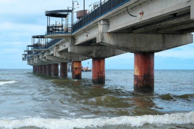 Uzakta, ağaçlarla ve güneşli mavi gökyüzüyle bir göl boyunca uzanan bir köprü görüntüsü. Güzel deniz manzarası. Köprü uzaklaşıyor..